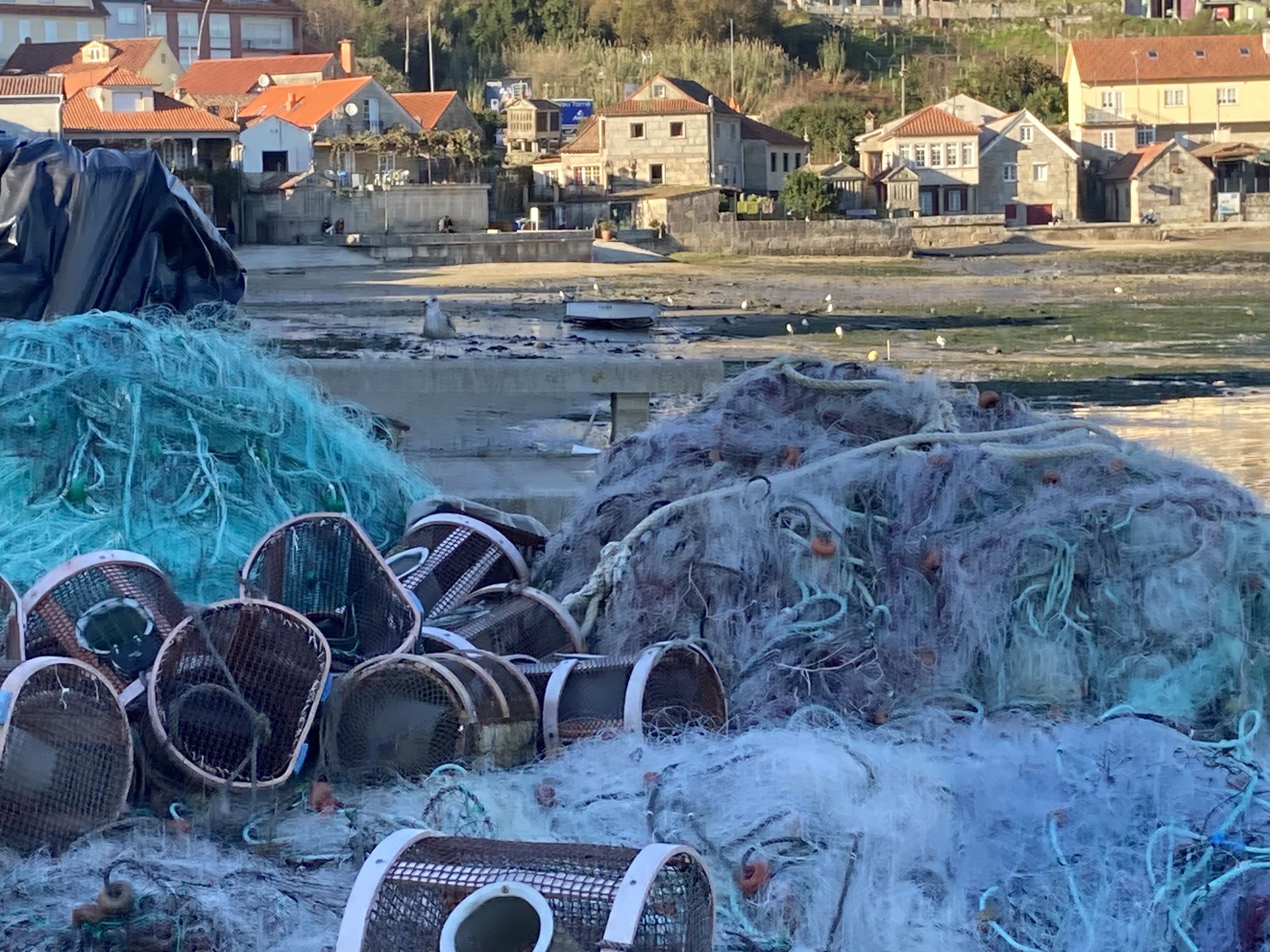fish net and lobster traps piled up in front of houses on a low tide port